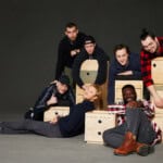 Gruppe junger Menschen mit Holzboxen, kreativ und fröhlich, in einem Studio.