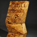 Holzskulptur mit markanter Maserung und moderner Form, präsentiert auf dunklem Hintergrund.