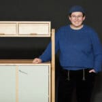 Frau mit Brille und Mütze neben modernem Holz- und Möbelstück.