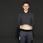 Handwerker hält ein Holzprodukt vor einem schwarzen Hintergrund, Fokus auf Holzverarbeitung.