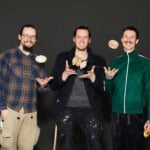 Drei Männer präsentieren kreative Holzkunstwerke und zeigen handwerkliches Können.
