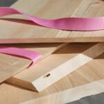 Holzplatten mit pinkem Gurtband und Leisten, Holzverarbeitung, nachhaltiges Holzdesign.