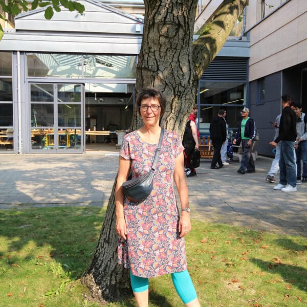 Frau Steht Lachend Unter Baum, Umgeben Von Urbaner Umgebung, Bei Holz Bewegt.